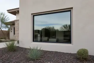 Finished picture window with clean caulk trim on a stucco wall and volcanic rock landscaping in Phoenix, AZ.