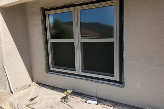 Newly installed window frame in a stucco wall at a job site in Phoenix, AZ, with tools on a drop cloth.