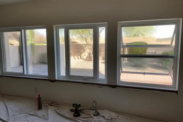 Window frame installation in a Phoenix, AZ home with tools on a drop cloth and desert landscaping visible outside.