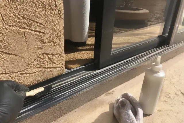 A contractor cleaning and lubricating a sliding window track on a sunny day in Phoenix, AZ.