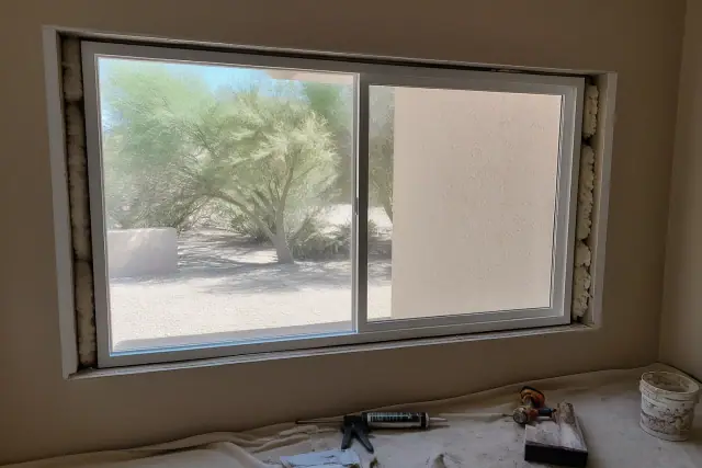 Sliding window frame installation in a Phoenix, AZ home with tools and materials on a drop cloth.