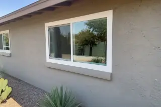 Cured caulk bead on a sliding window frame at a stucco home in Phoenix, AZ, with a desert xeriscape yard.