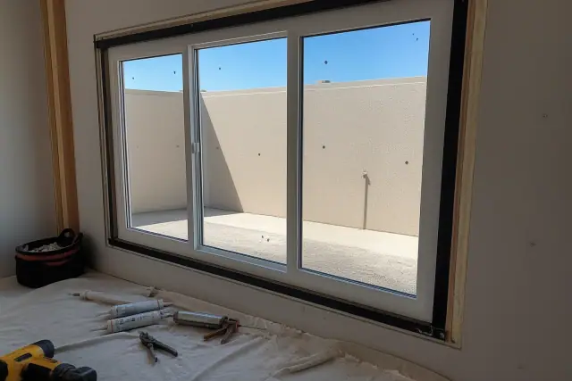 A commercial window frame installation in progress on a stucco wall in Phoenix, AZ, with tools on a drop cloth.