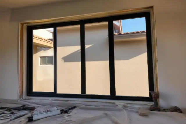 Thermally broken aluminum window frame installation in a Phoenix, AZ stucco wall with tools on a drop cloth.