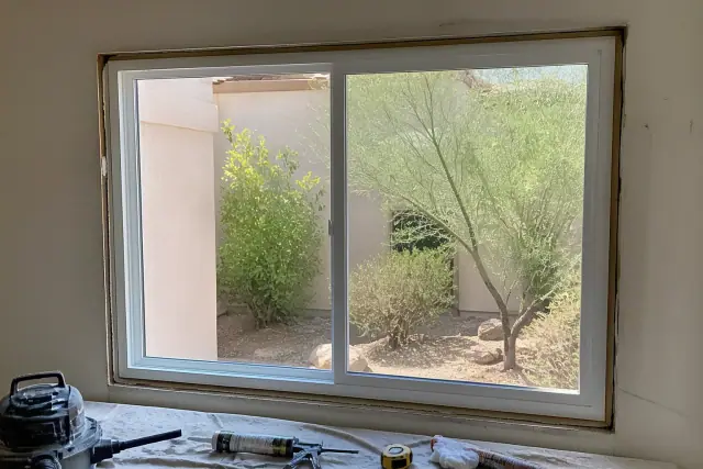 Vinyl sliding window installation in progress on a stucco home in Phoenix, AZ, with tools visible on a drop cloth.