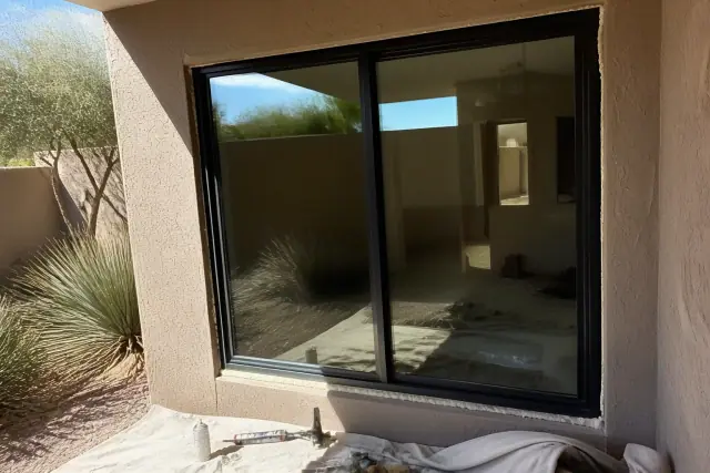 A west-facing window installed in a stucco wall under harsh summer sun in Phoenix, AZ, with tools on a jobsite drop cloth.