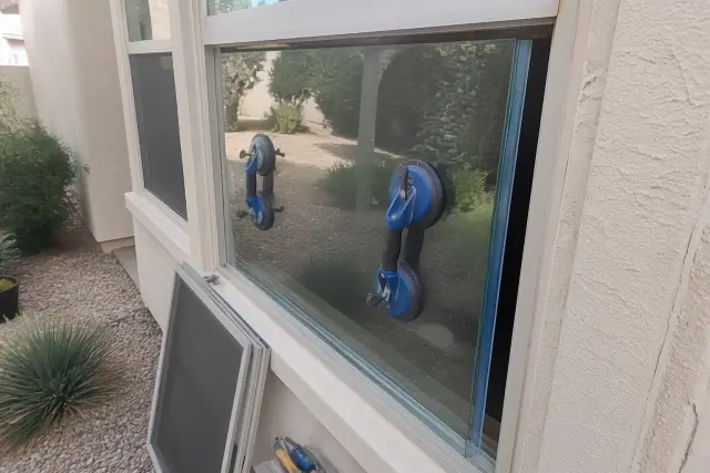 Technician using suction tools to install a replacement glass window pane in a Gilbert, AZ home.