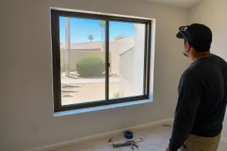 Worker inspecting a finished window installation in a stucco home with desert views in Phoenix, AZ.