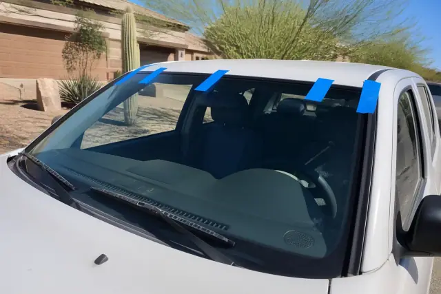 New windshield with retention tape on a vehicle in Phoenix, AZ, with desert landscaping in the background.