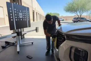 Technician cleaning a sensor on a car near a calibration stand in a Phoenix, AZ service bay.