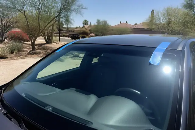 Newly installed windshield with retention tape on a vehicle in a Phoenix, AZ desert yard.