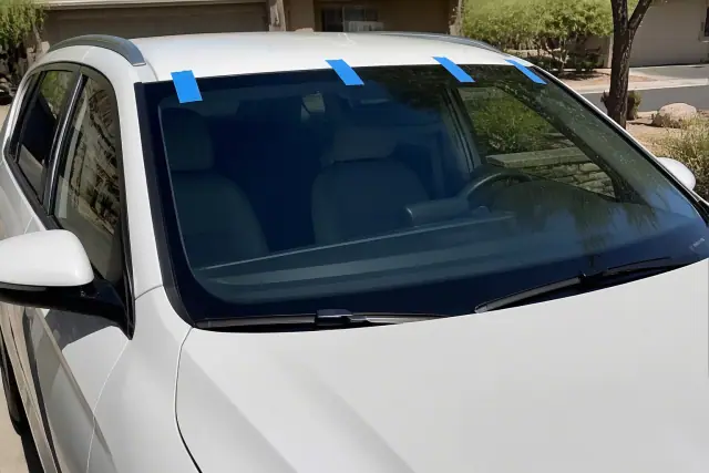 Newly installed windshield with retention tape on a car parked in an Avondale, AZ driveway.