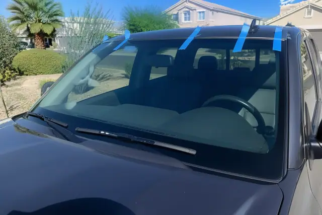 Newly installed car windshield with retention tape on a vehicle in a xeriscaped yard in Gilbert, AZ.