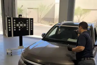 Technician inspecting a new windshield with retention tape in a Phoenix, AZ service bay.