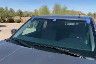 A newly installed windshield with blue retention tape on a car parked in a dusty desert setting in Phoenix, AZ.