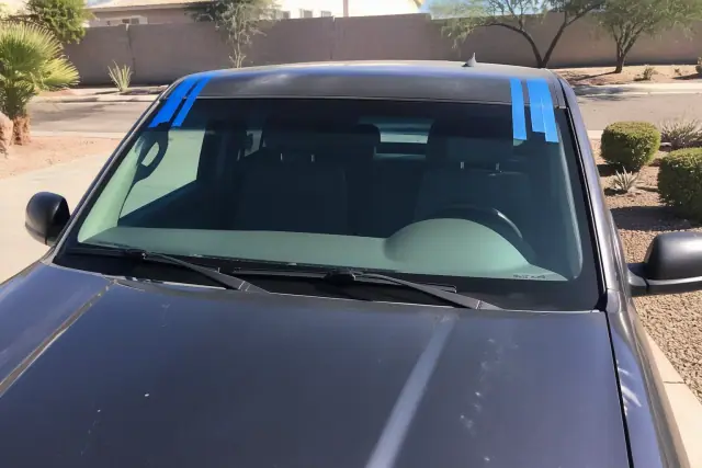 A newly installed windshield with retention tape on a car parked in a xeriscaped lot in Mesa, AZ.