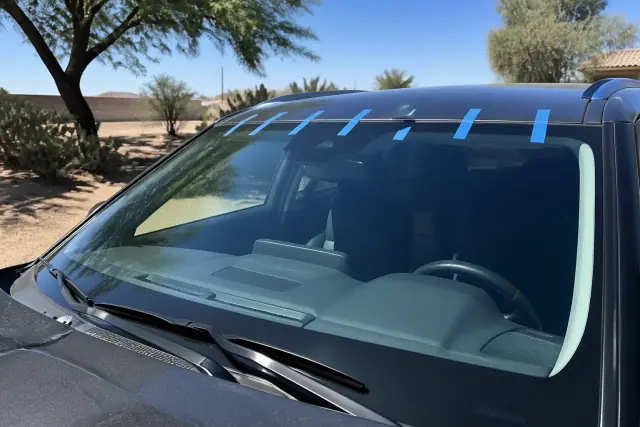 New windshield installed with retention tape on a car parked in a dry, sunny lot in Goodyear, AZ.