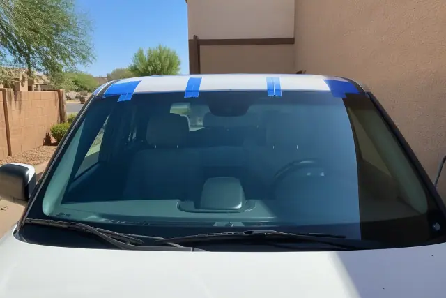 A newly installed windshield with retention tape on a vehicle parked against a stucco wall in Gilbert, AZ.