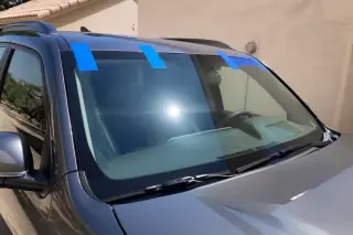 Car windshield with blue retention tape applied across the top, parked in a sunny driveway in Phoenix, AZ.