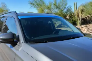 Car with a newly installed windshield and retention tape parked in a sunny xeriscaped yard in Phoenix, AZ.