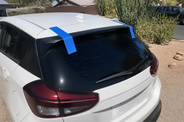 A hatchback with a newly installed rear window held by retention tape on a sunny driveway in Phoenix, AZ.