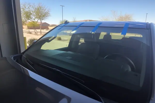 Newly installed car windshield with retention tape in a service bay under bright sun in Chandler, AZ.