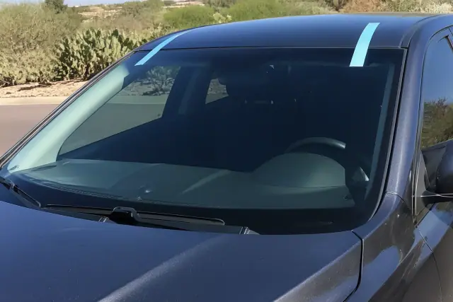 Newly installed car windshield with retention tape in a Scottsdale, AZ service bay with prickly pear cactus outside.
