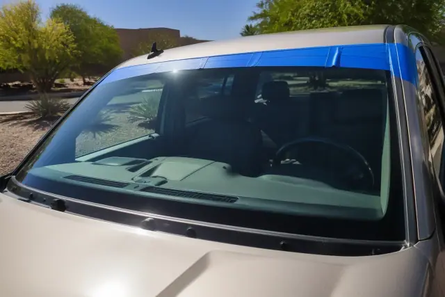 Newly installed car windshield held by retention tape in Phoenix, AZ, with desert landscaping in the background.