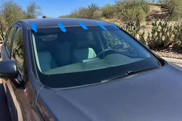 New windshield secured with retention tape on a car parked in Mesa, AZ, with prickly pear cacti in the background.