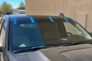 Newly installed car windshield with retention tape against a sunlit stucco wall in Phoenix, AZ.