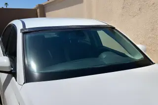 Car with a newly installed windshield and retention tape parked against a stucco wall in Phoenix, AZ.