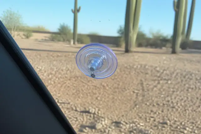 Resin injector tool repairing a small windshield chip in Phoenix, AZ with desert gravel and cacti in the background.