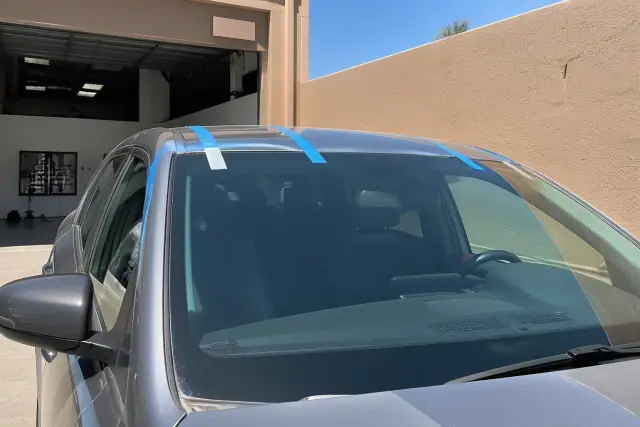 Newly installed windshield with retention tape on a vehicle in a Phoenix, AZ service bay.