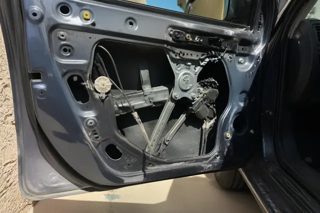 Frayed window regulator cable and misaligned pulley inside an open car door at a repair shop in Phoenix, AZ.