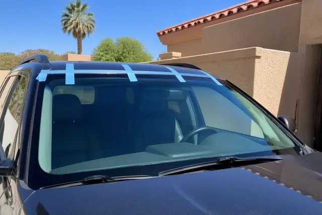 Newly installed windshield with retention tape on a vehicle parked outside a stucco building in Phoenix, AZ.