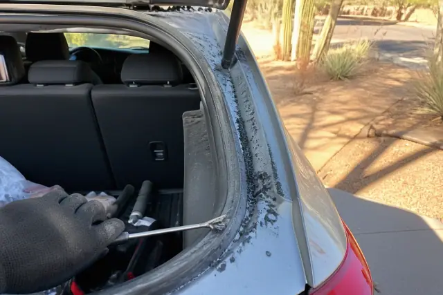 Technician removing broken rear glass fragments from a hatchback trunk in Phoenix, AZ.