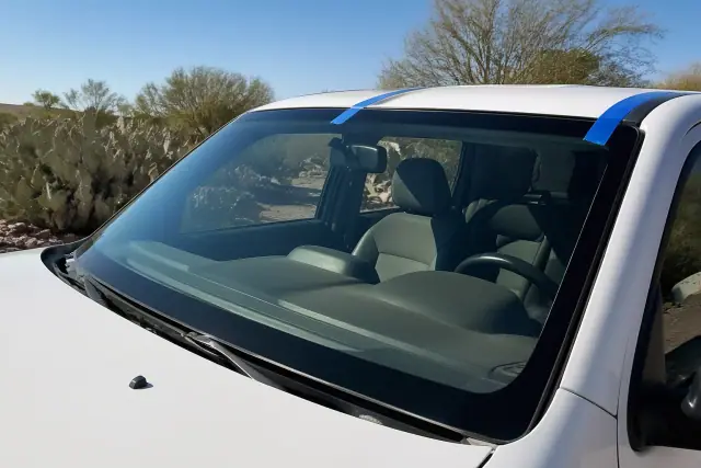 A newly installed car windshield with retention tape on a vehicle in Phoenix, AZ, with desert cacti in the background.