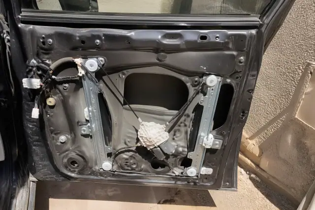 Open car door interior showing a window regulator assembly and electric motor during repair in Phoenix, AZ.
