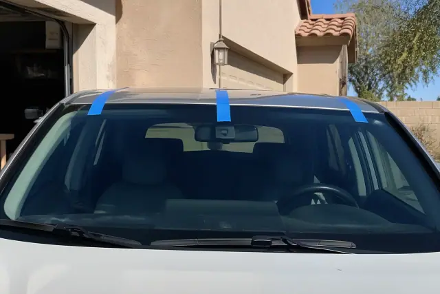 New windshield installed on a vehicle at a residential driveway in Gilbert, AZ, held in place with retention tape.