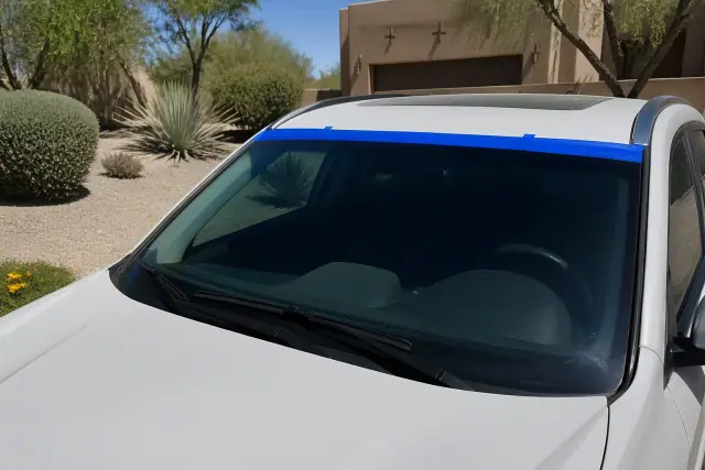 Newly installed windshield with retention tape on a car parked in a gravel driveway in Phoenix, AZ.