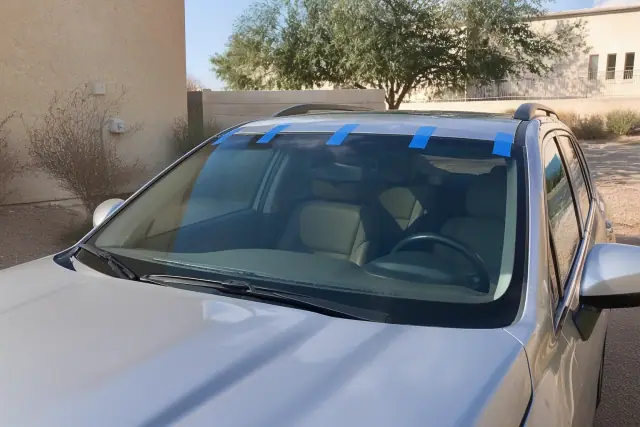 New windshield with retention tape on a car parked outside a stucco building in Phoenix, AZ.