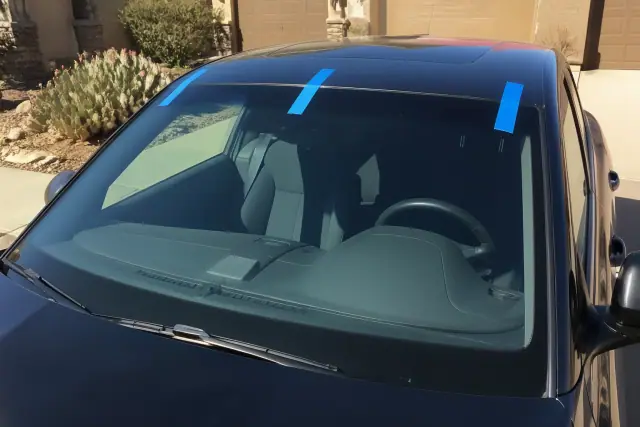 Newly installed car windshield with retention tape in a sunny Goodyear, AZ driveway with prickly pear cactus landscaping.