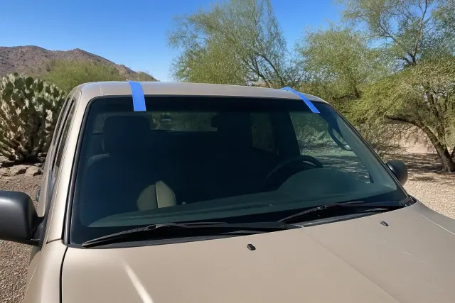 Newly installed car windshield held by retention tape in a Phoenix, AZ driveway.