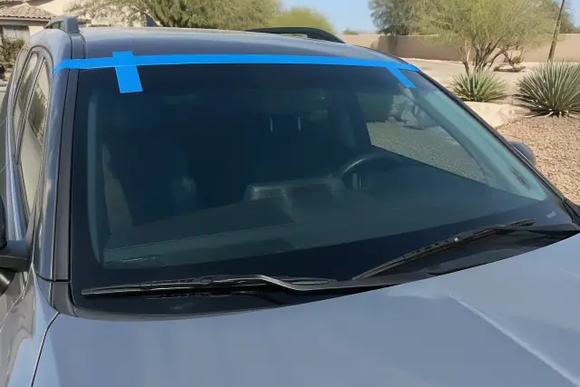 New windshield with retention tape on a car parked in front of xeriscape landscaping in Mesa, AZ.