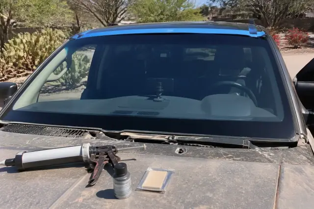 Windshield held by retention tape on a vehicle in Paradise Valley, AZ, with primer tools and Sonoran desert landscaping.