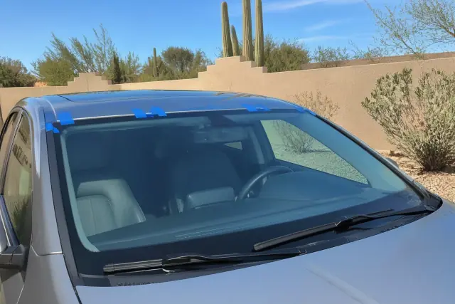 Newly installed vehicle windshield with retention tape in Tempe, AZ, featuring desert saguaro cactus and stucco walls.