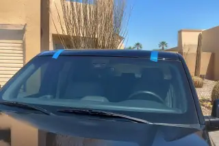 Car with a new windshield and retention tape parked in front of a stucco building in Phoenix, AZ.