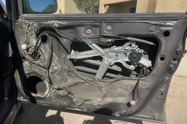 Exposed car door window regulator and electric motor being repaired in Phoenix, AZ.