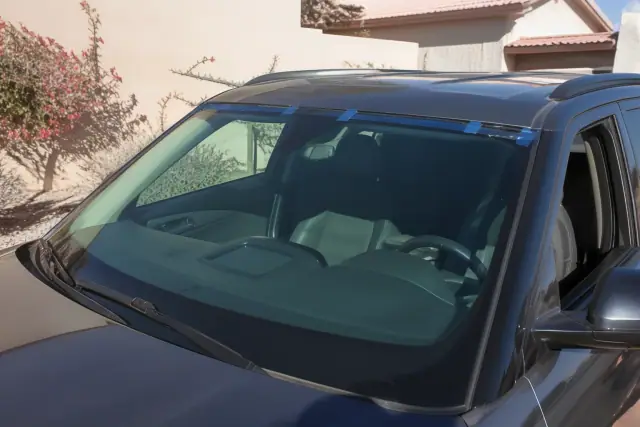 Newly installed car windshield with curing tape on a vehicle in Phoenix, AZ, parked against a stucco wall.