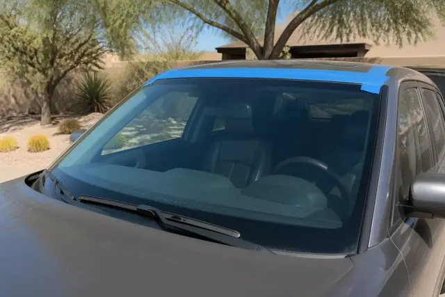 Newly installed car windshield with retention tape in Phoenix, AZ, set against desert landscaping.